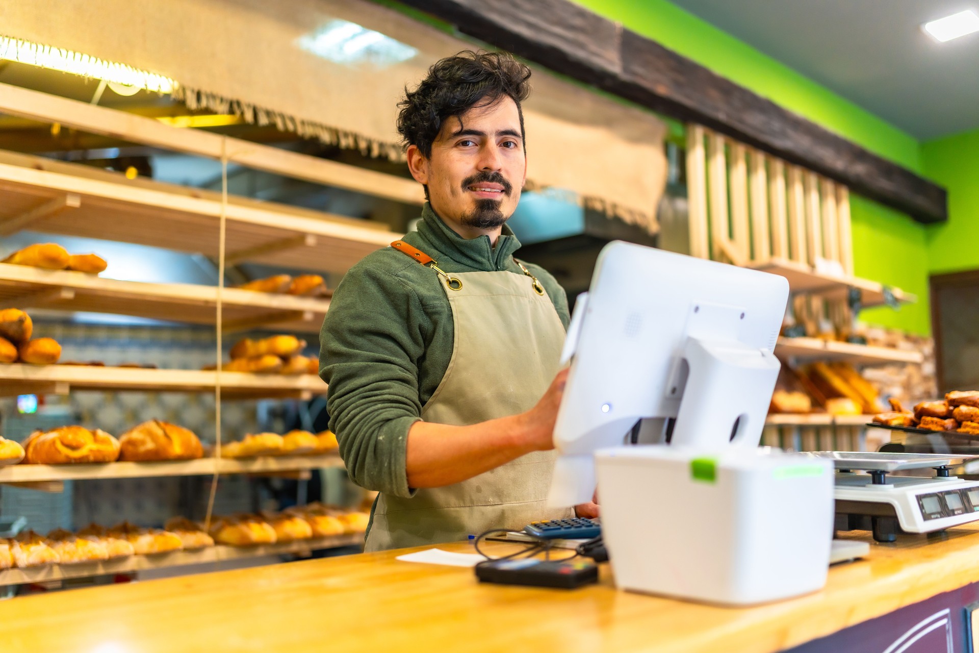 Salesman using computer stranding at counter of a bakery shop Salesman using computer stranding at counter of a bakery shop
